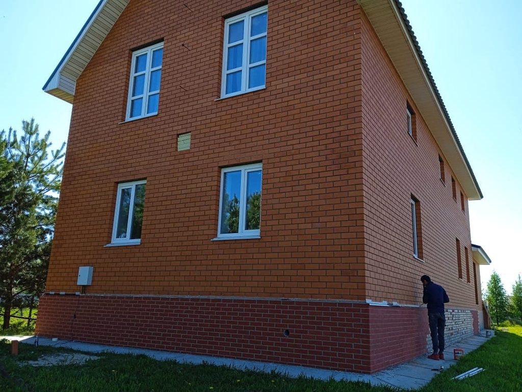 Отделка цоколя коттеджа в Полково красным гибким кирпичом в процессе монтажа